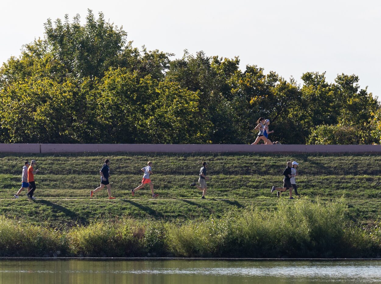 Fans run below the race course to follow the lead runners during the 5A girls’ 3200m race at...