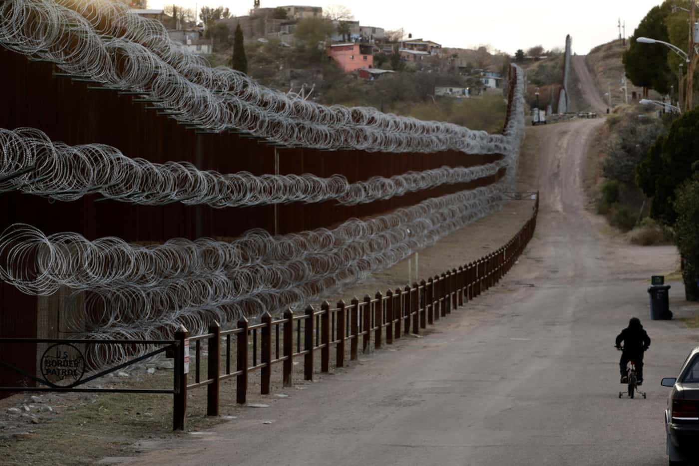 A boy rides his bike along a razor-wire-covered border wall that separates Nogales, Ariz....