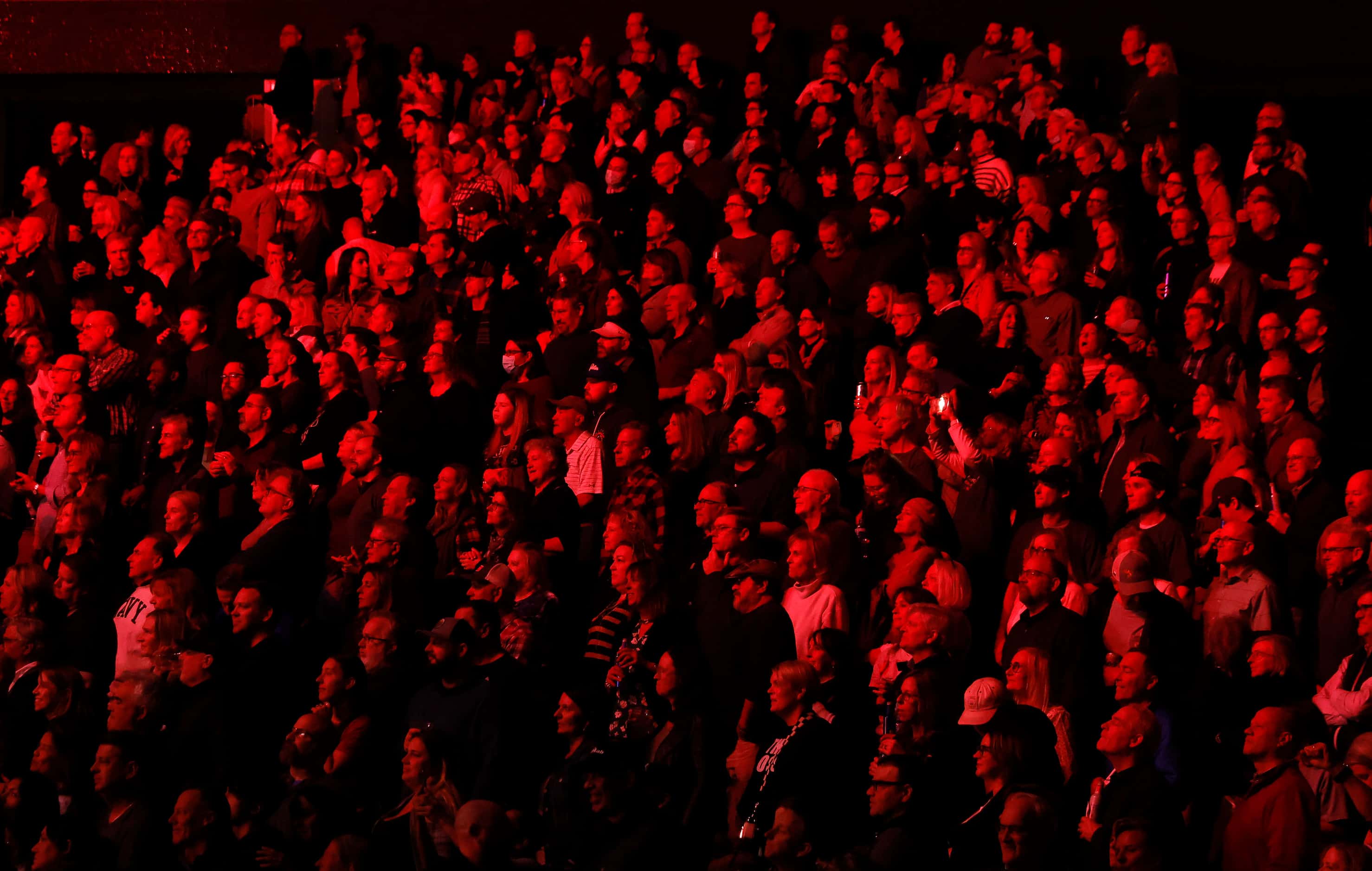 Bathed in red light from the stage, fans watch Bruce Springsteen perform with the E Street...