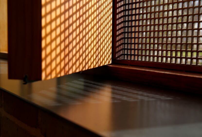 Morning light filters through a perforated steel screen, casting shadows onto a wooden vent...