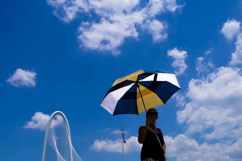 Vimarie Rivera shields herself from the sun as she walks on the Ronald Kirk Bridge, with the...