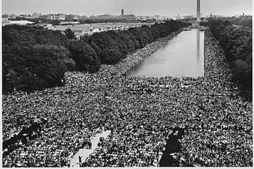 A wide-angle view shows marchers along the National Mall at the Reflecting Pool and the...