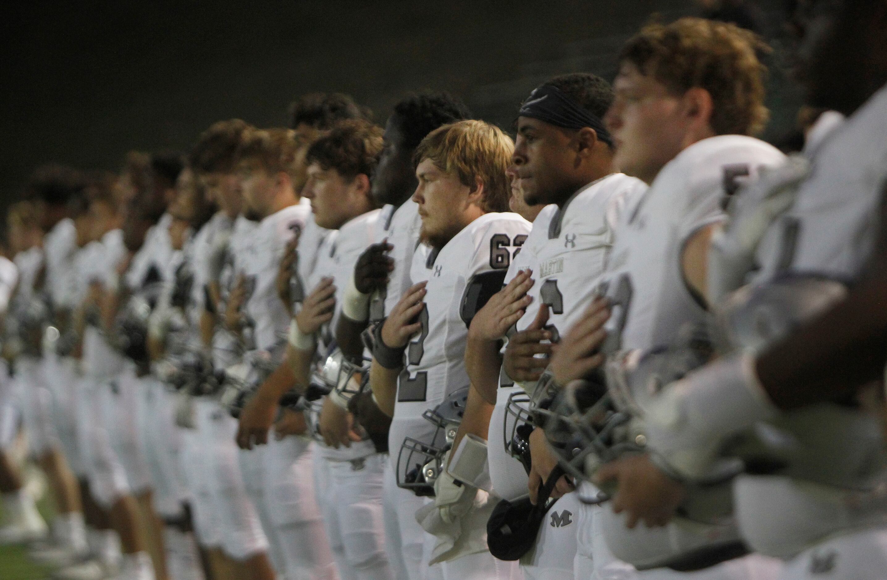 Members of  Arlington Martin pause for the playing of the national anthem prior to the...