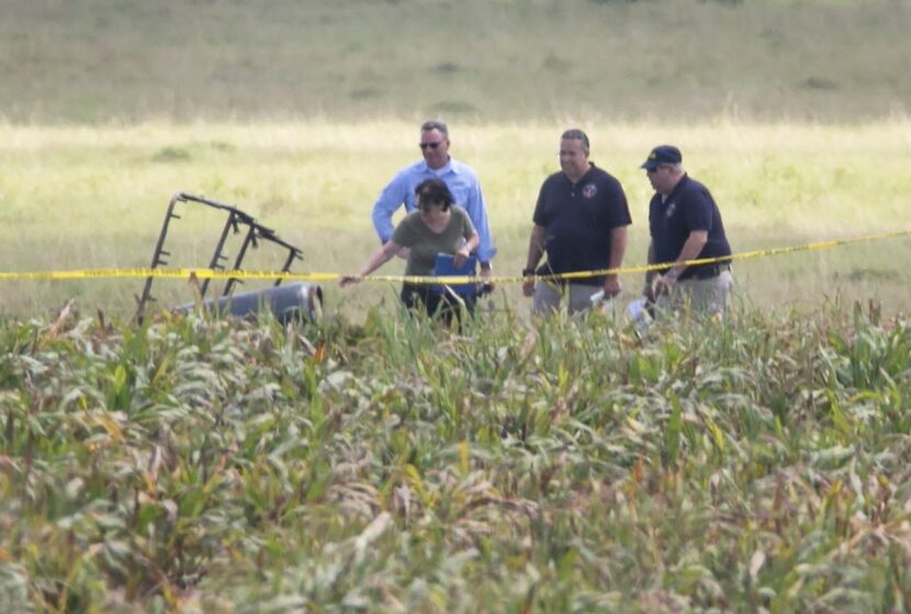 The partial frame of a hot air balloon is visible above a crop field as investigators comb...