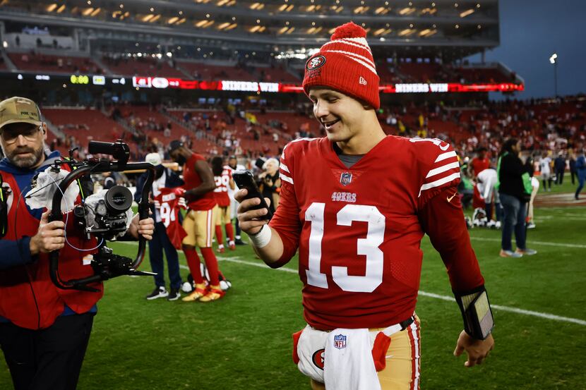 San Francisco 49ers quarterback Brock Purdy (13) holds a cell phone as he walks on the field...