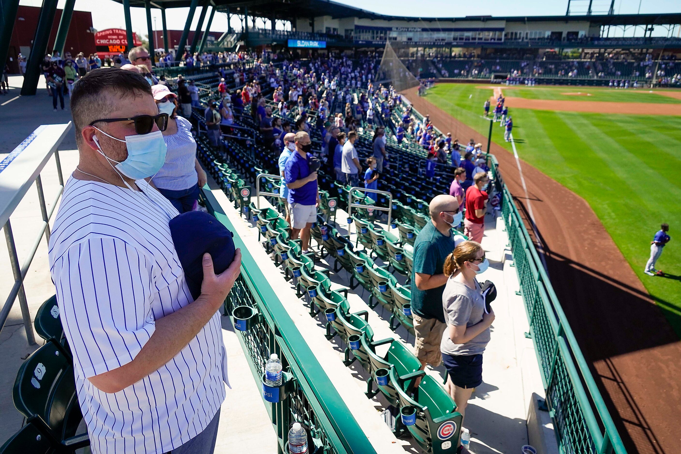 Fans relax stand for the national anthem before a spring training game between the Texas...