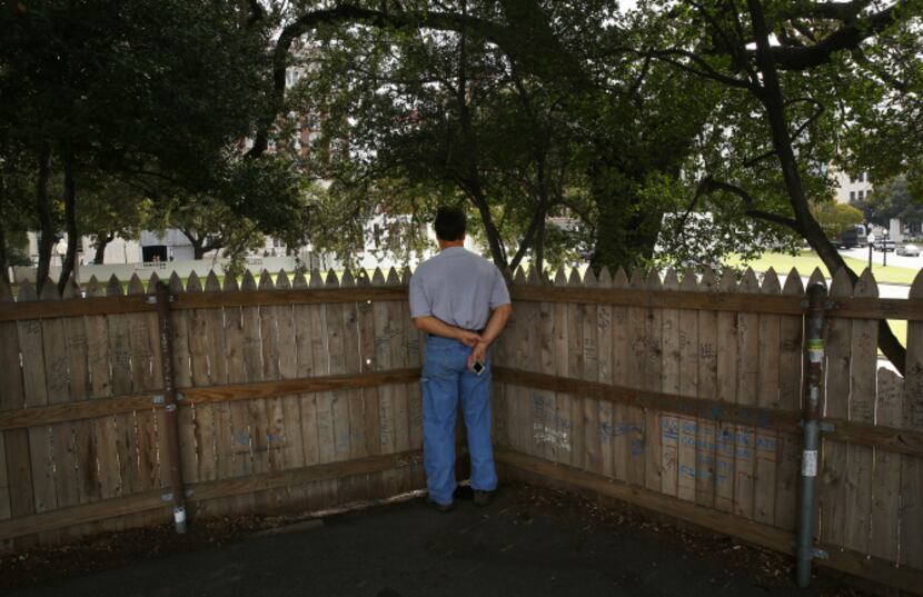 A tourist views the JFK assassination site from behind a graffiti-covered fence atop the...