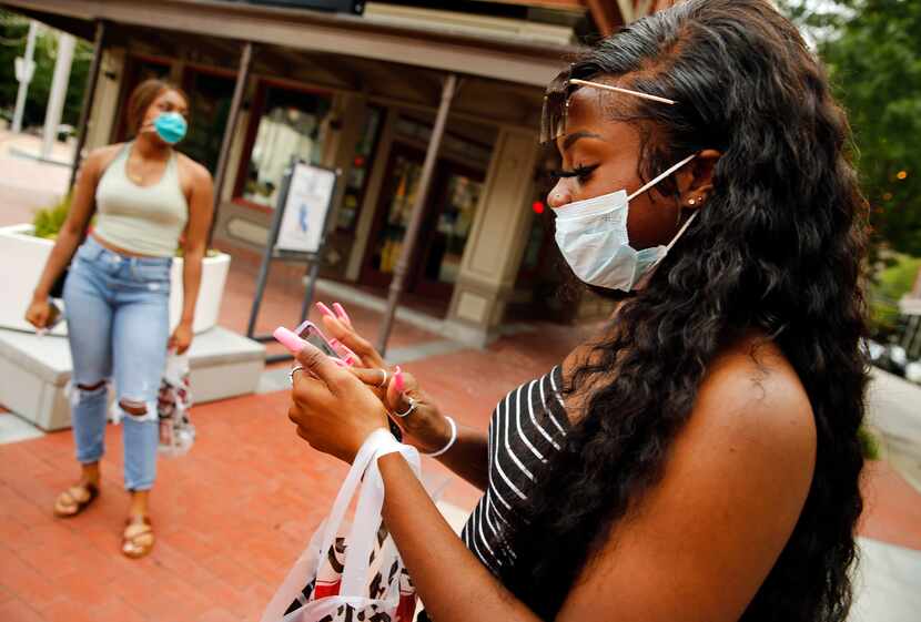 Donning a mask, Nicole Obialo of Coppell, Texas checks her phone as she and her girlfriends...