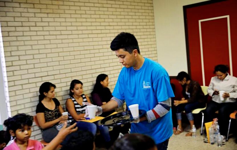 
Tony Nicanor hands out cups of Pedialyte to children after a bus full of migrants arrived...