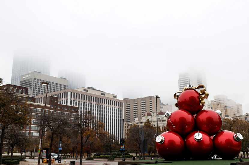 Red Christmas ornaments sit near the Omni Dallas Hotel as fog looms over the city skyline of...