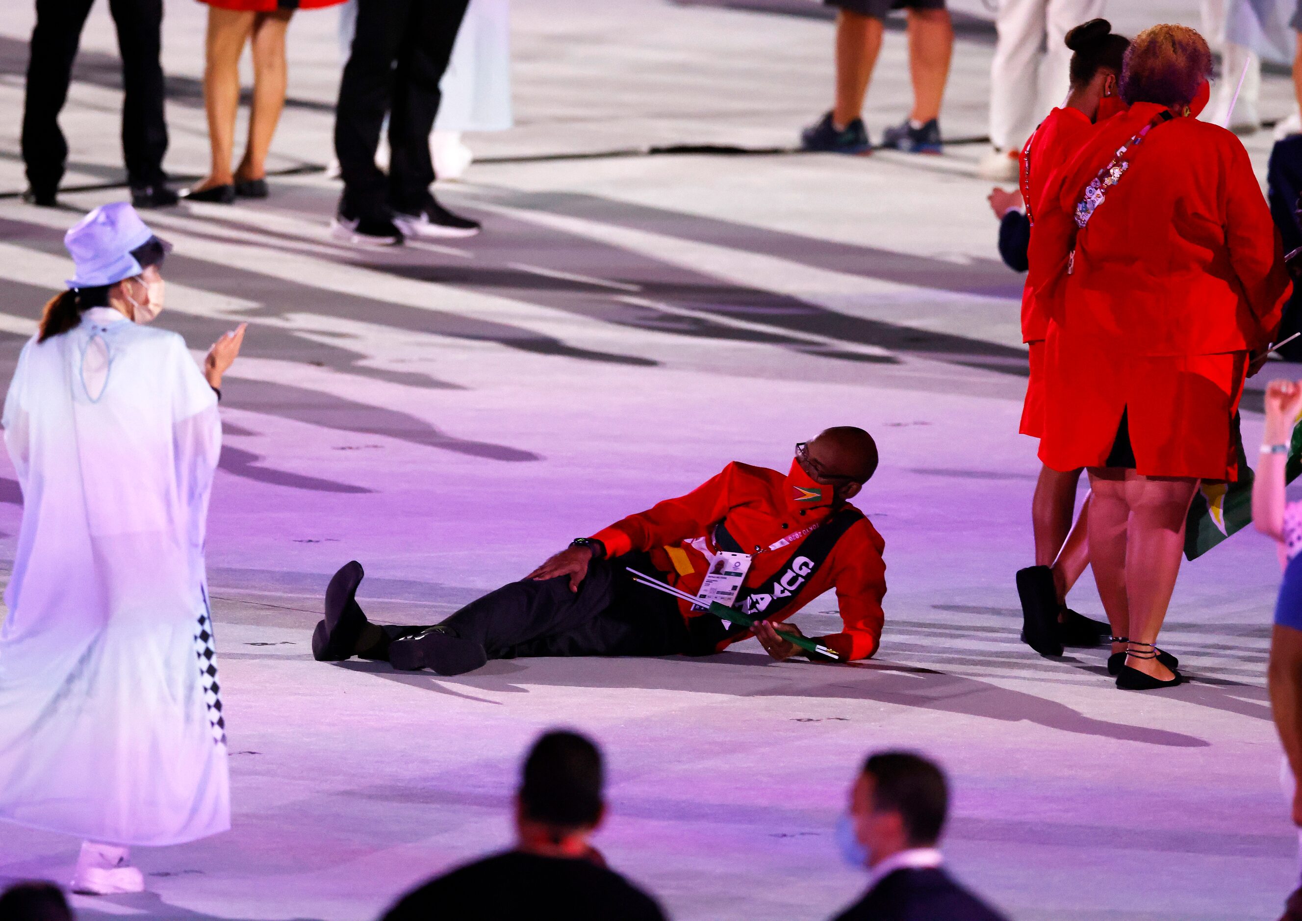 A Guam athlete rests on the ground as teams are introduced during the opening ceremony for...