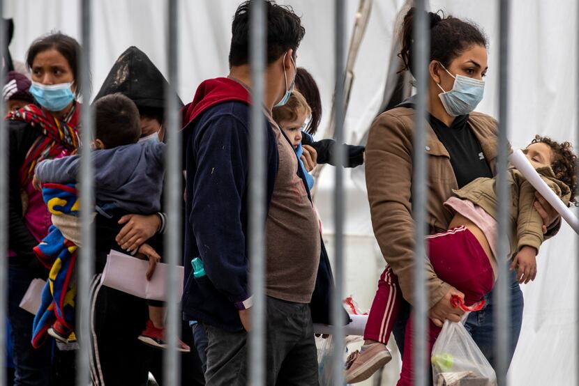 A woman carrying a small child waits in line with other migrant families to be tested for...