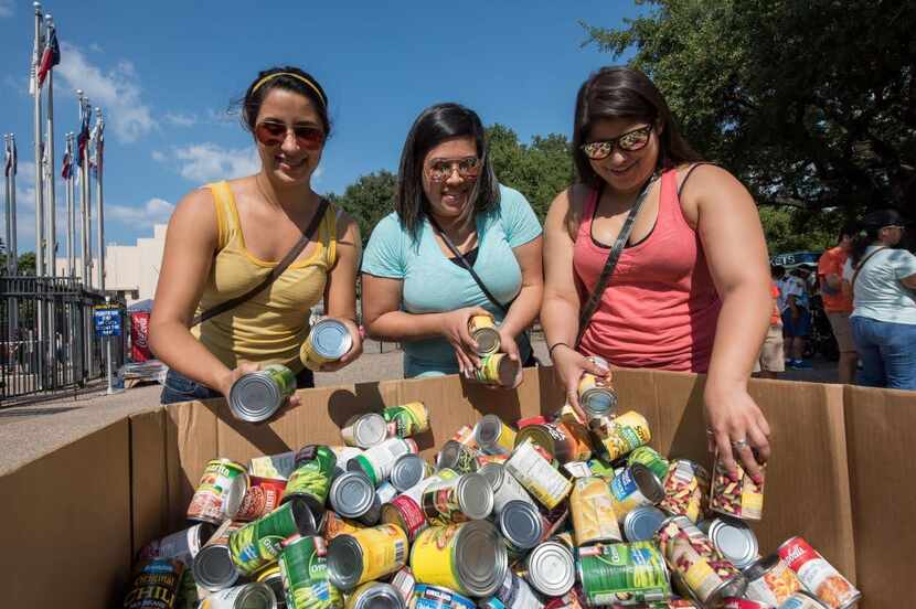 Three women drop off cans of food in a large box at the State Fair of Texas