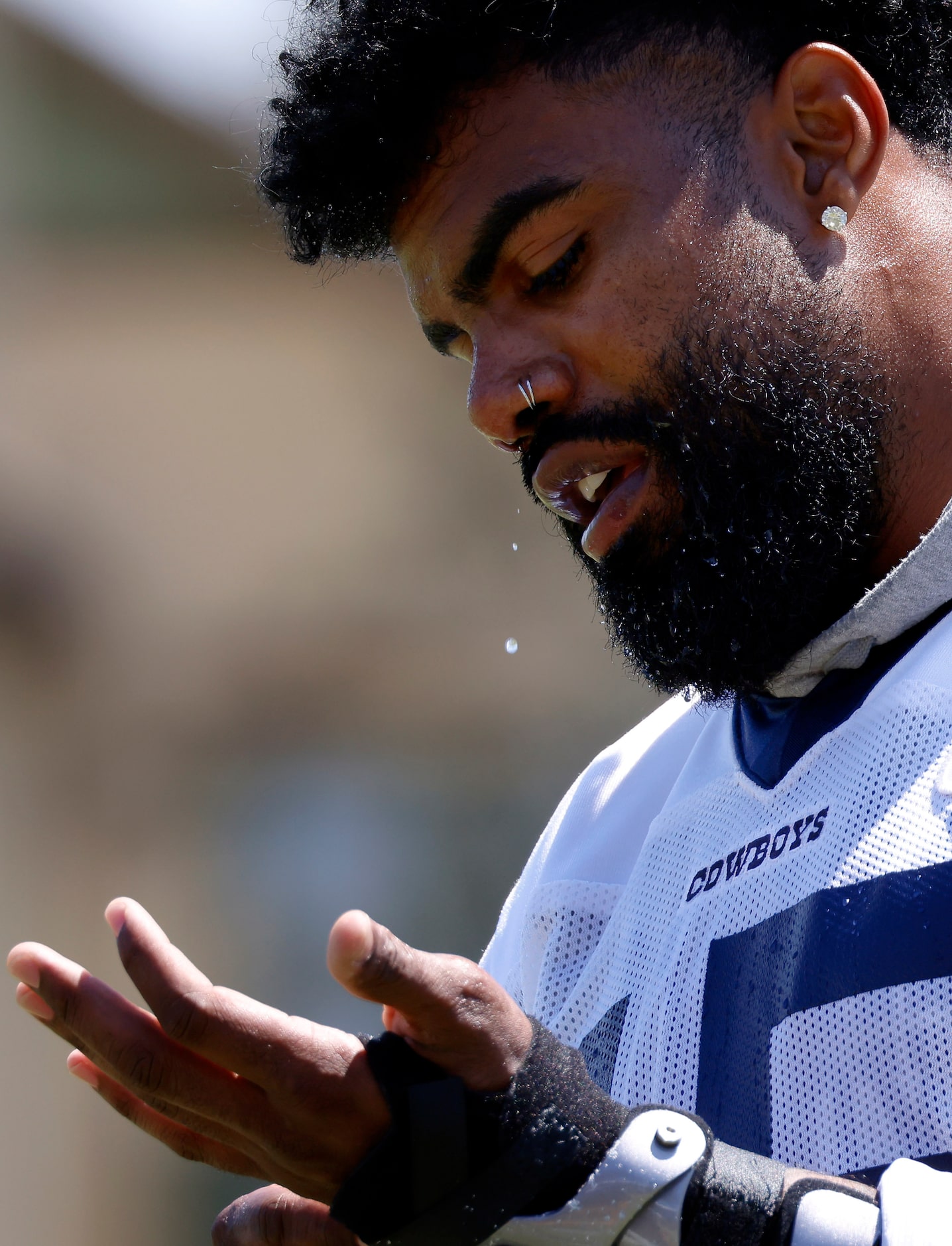 Sweat drips from Dallas Cowboys running back Ezekiel Elliott’s nose as he wraps his hands...