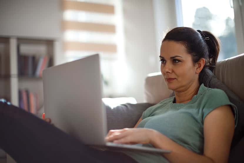 A woman on a couch looks at her laptop.