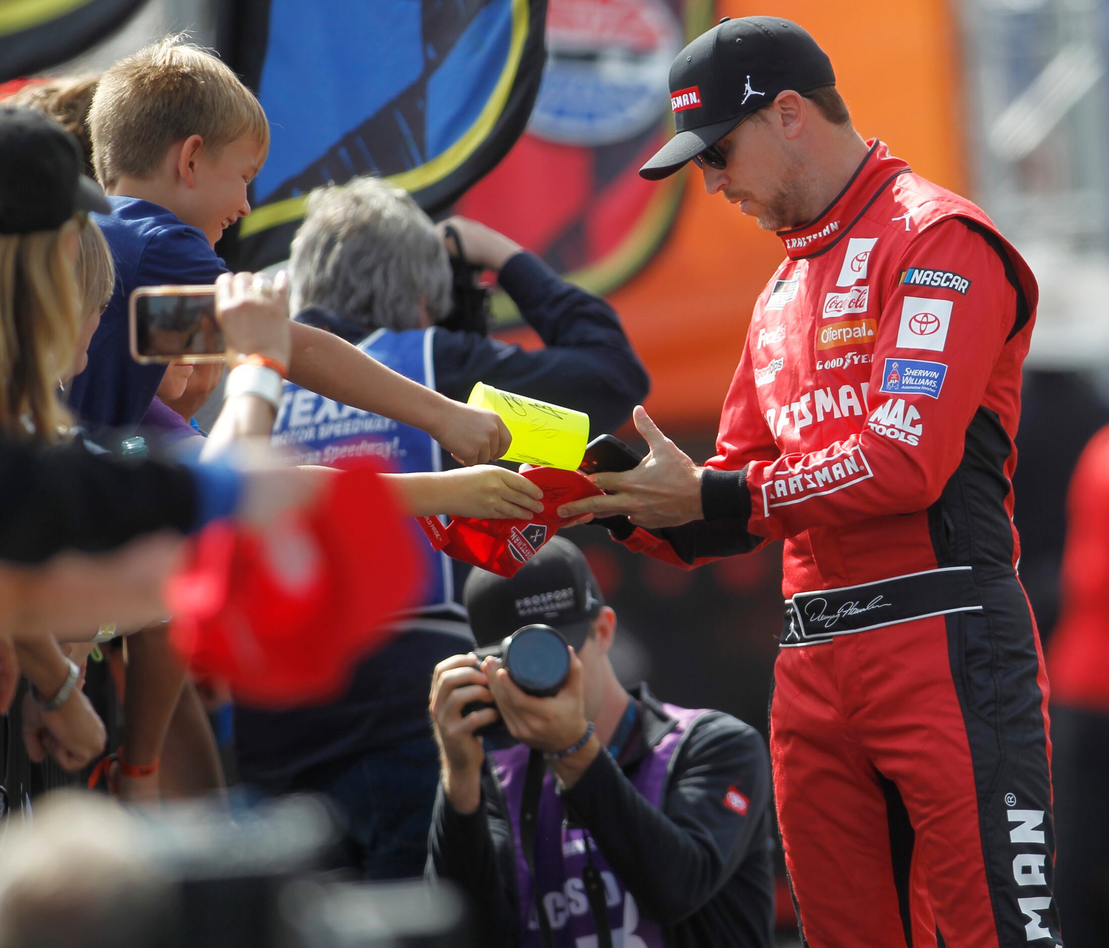 Driver Denny Hamlin pauses to sign an autograph to the delight of a young race fan during...
