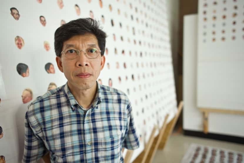 Rev. Martin Nguyen C.S.C. in front of an ongoing project involving a series of faces painted...