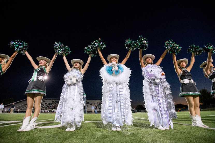 Members of the Southlake Carroll Emerald Belles drill team sport giant mums before a high...