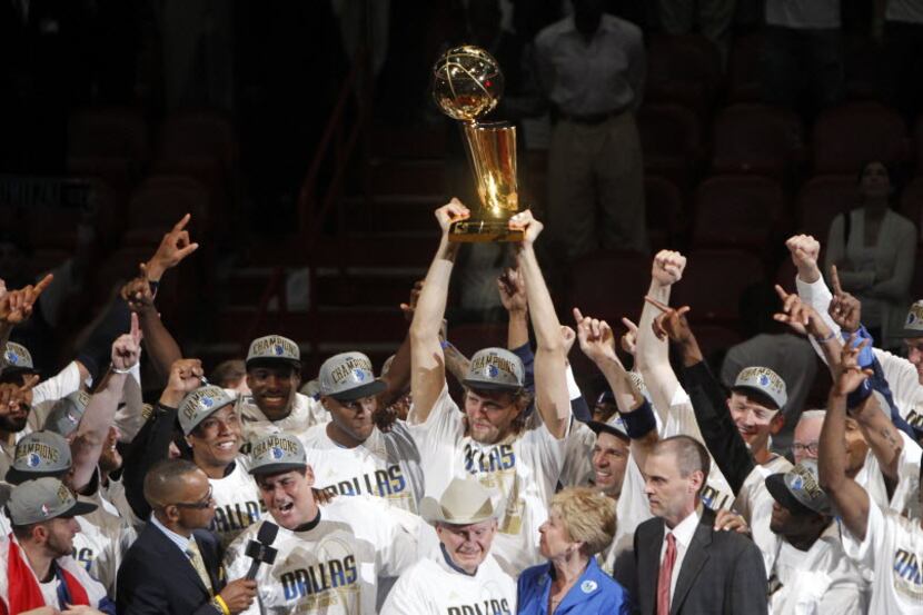 Dirk Nowitzki holds up the NBA Championship Larry O'Brien trophy, as he, Mark Cuban (being...