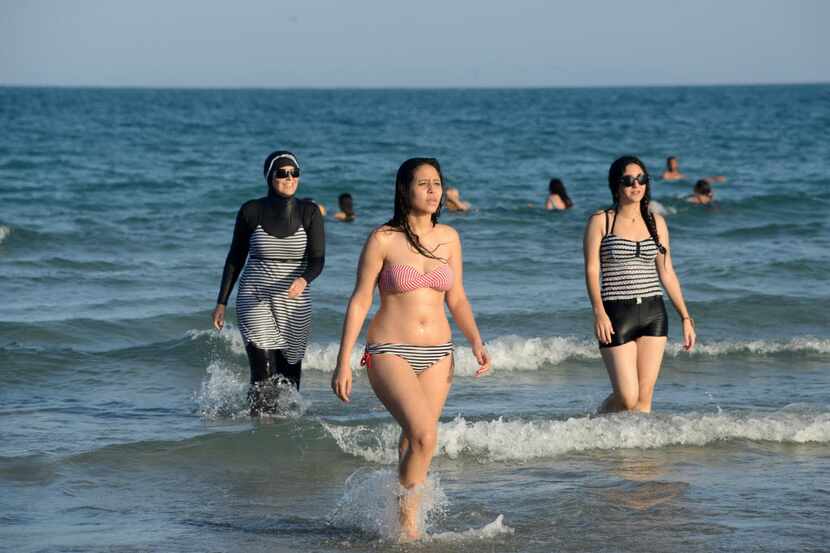 Tunisian women, one on the left wearing a burkini, walk in the water on August 16, 2016 at...