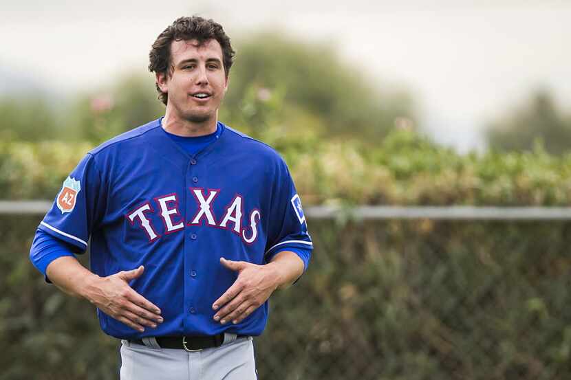 Rangers pitcher Derek Holland grabs at his belly while motioning to reporters during the...