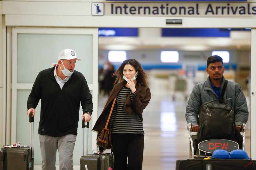 Travelers, some seen wearing protective masks, arrive Jan. 28 in the international arrivals...