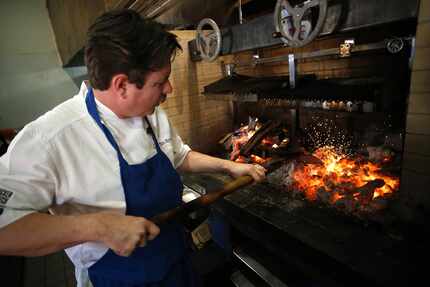 Chef Tim Byres prepares to cook an Eisenhower steak by stoking the coals he'll put the steak...