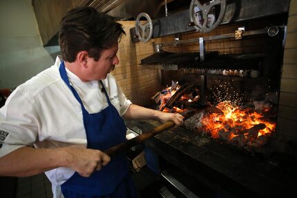 Chef Tim Byres prepares to cook an Eisenhower steak by stoking the coals he'll put the steak...