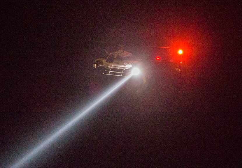  A helicopter with a search light circles as police officers gather at the intersection of...