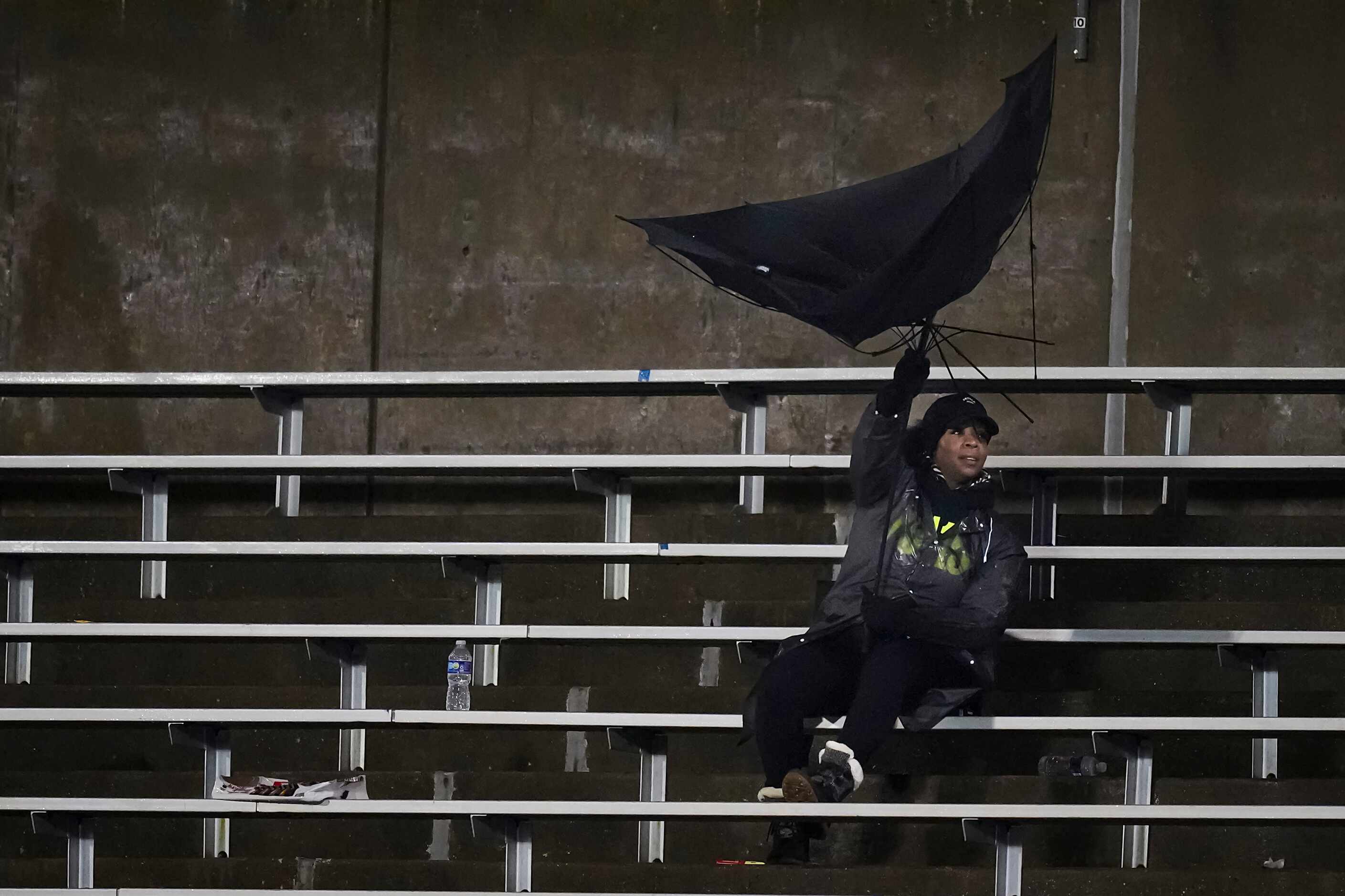 A fan struggles with an umbrella in the wind during the second half of a District 11-6A high...