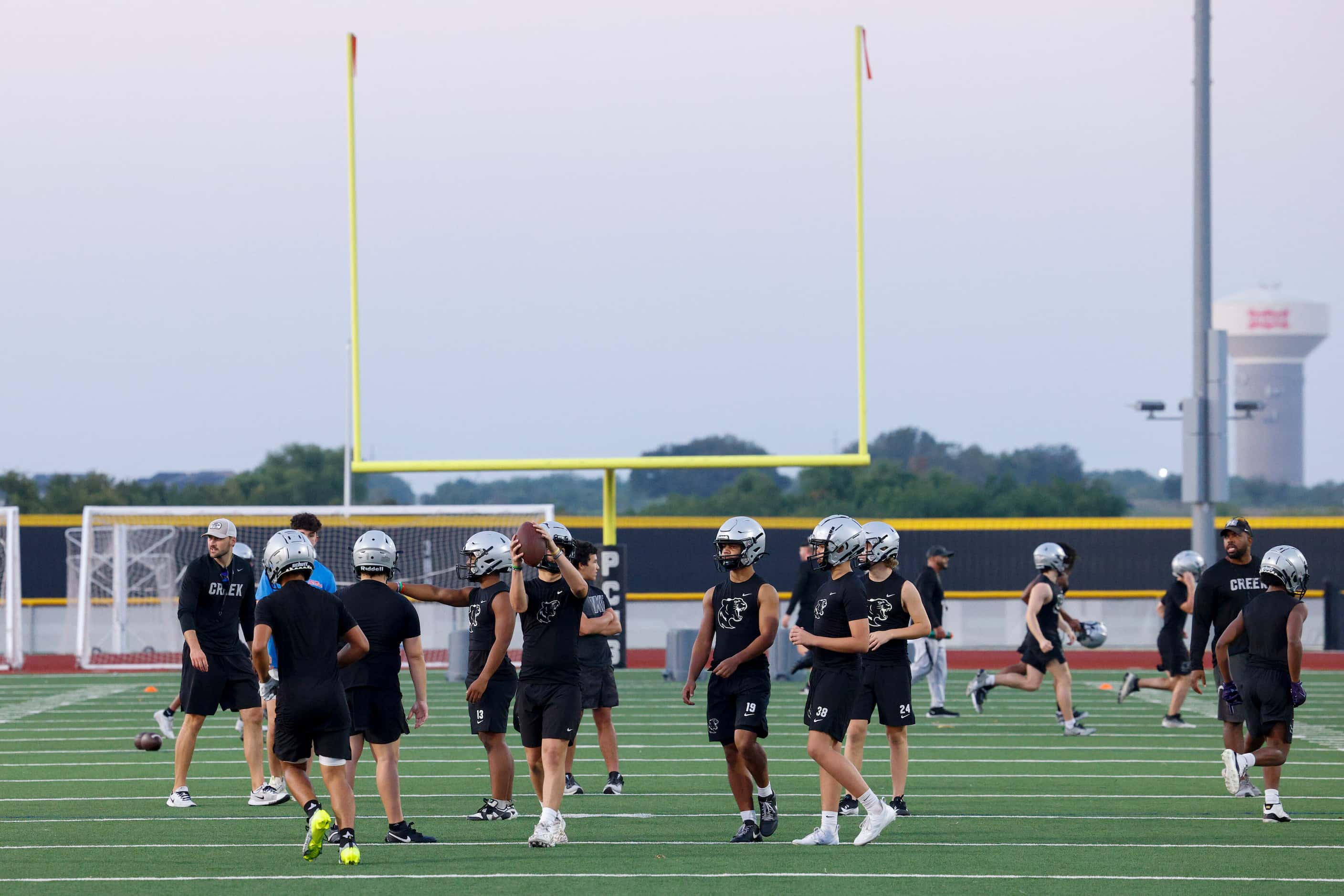 Football players walk on the field during an early morning practice at Panther Creek High...