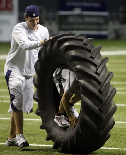 Dallas Cowboys equipment intern Brett Buchanan moves a big tire as John Stephen Jones rides...