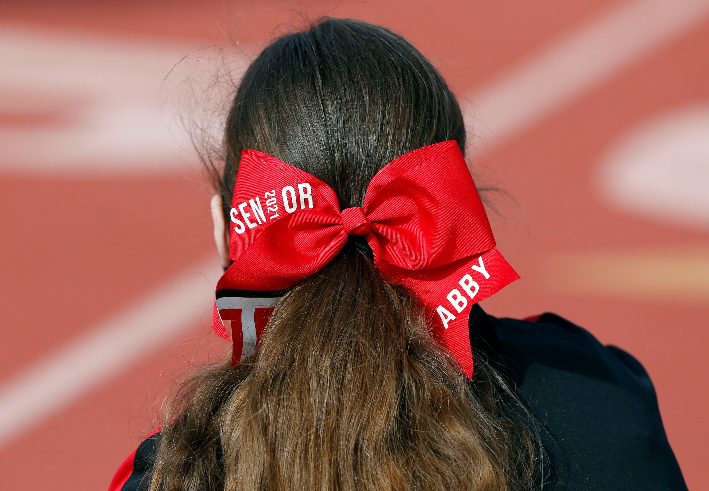North Garland cheerleader “Abby”, a “Senior 2021” sports a customized red hair bow before...