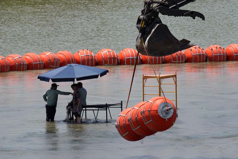 Workers take a break from deploying a large buoys in the Rio Grande near Eagle Pass, Texas,...