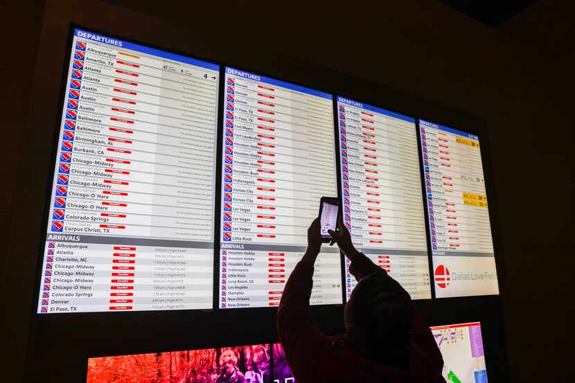 A traveler takes a photo with their cellphone of the Departures/Arrivals board that shows...