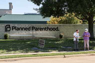 A couple of protesters stands on the sidewalk near Planned Parenthood next to anti-abortion...