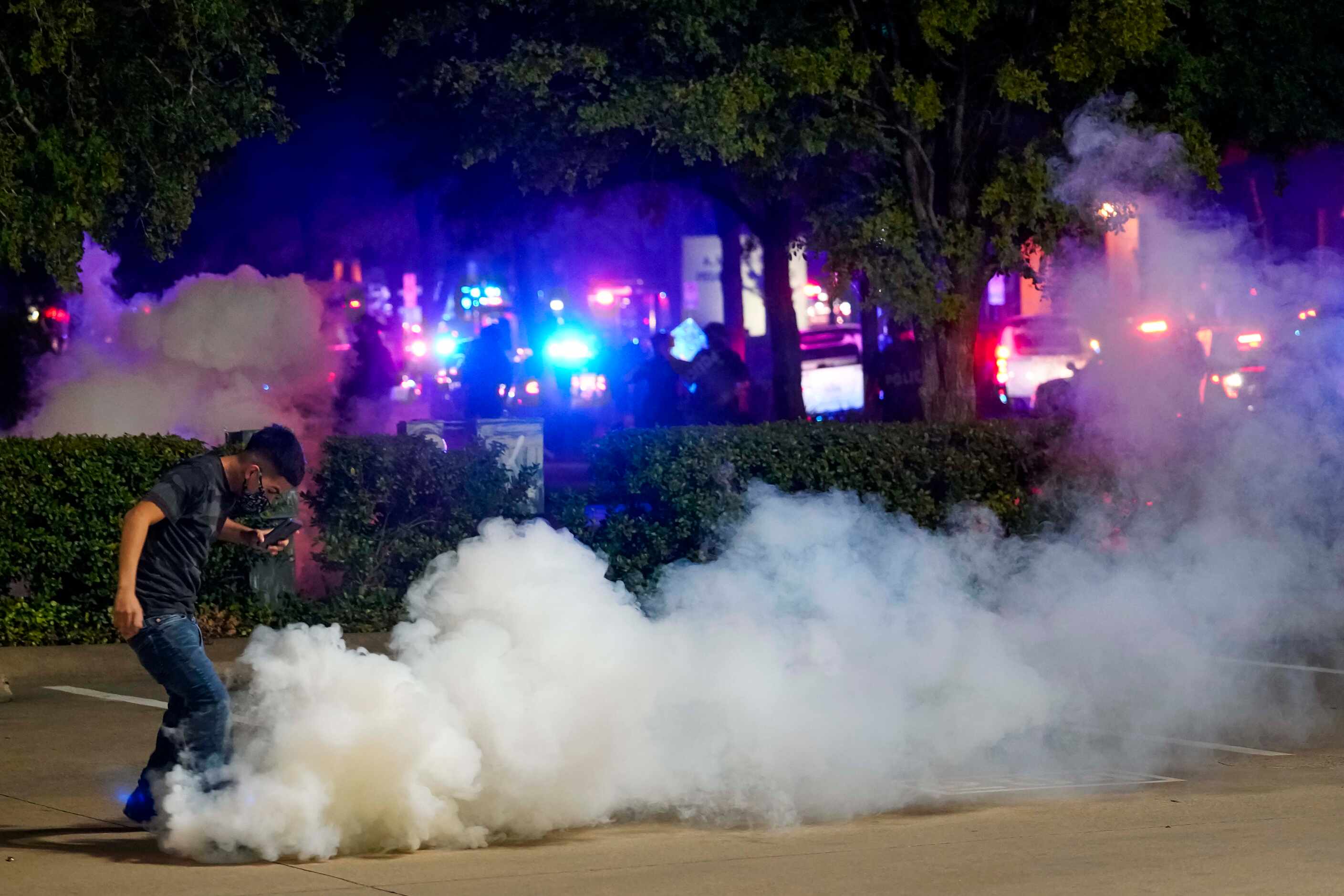 A protester tries to kick away a canister of teargas after it landed at his feat as Dallas...