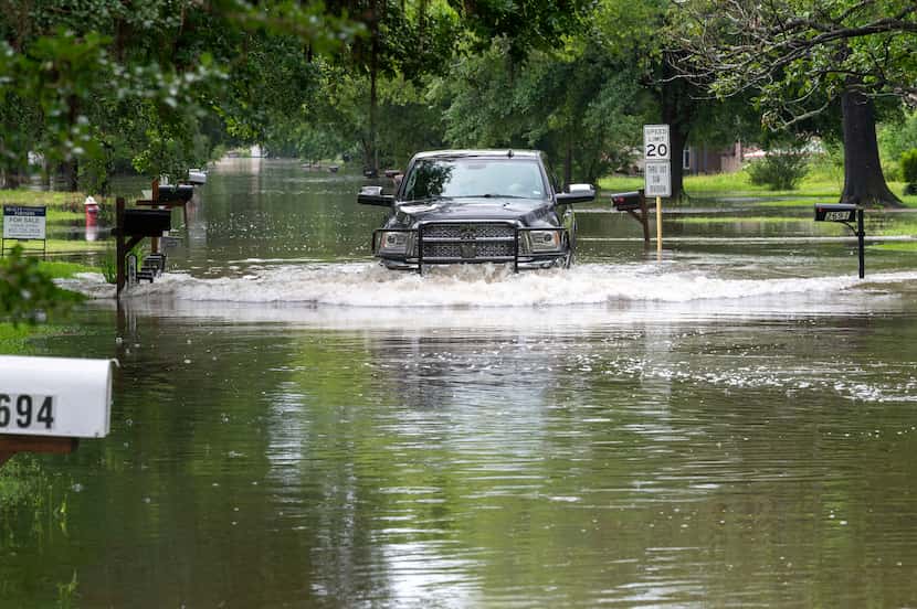 A pickup truck maneuvers a residential street filled with water in Woodloch, Texas,...