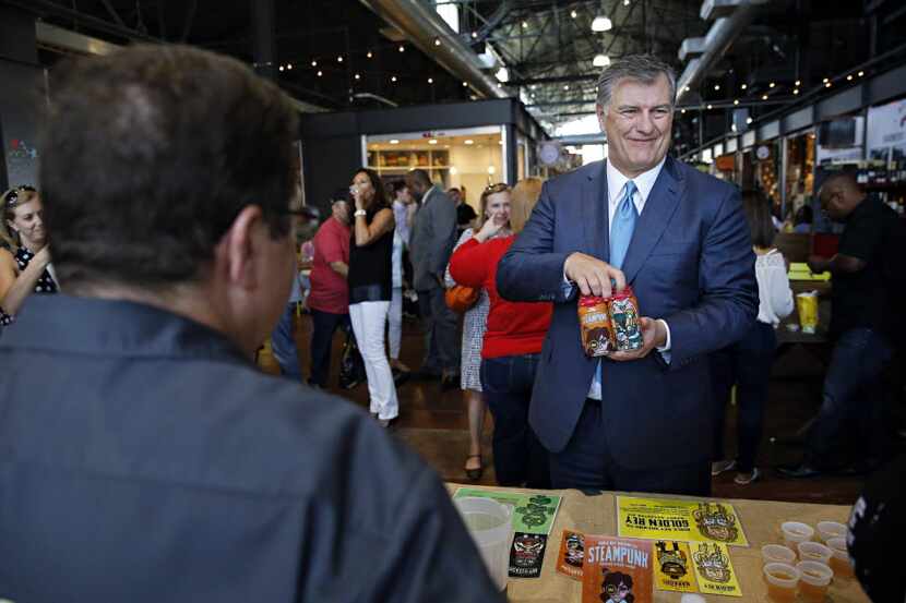Dallas Mayor Mike Rawlings (right) smiles after getting a sample six-pack from Ken Rigoulot...