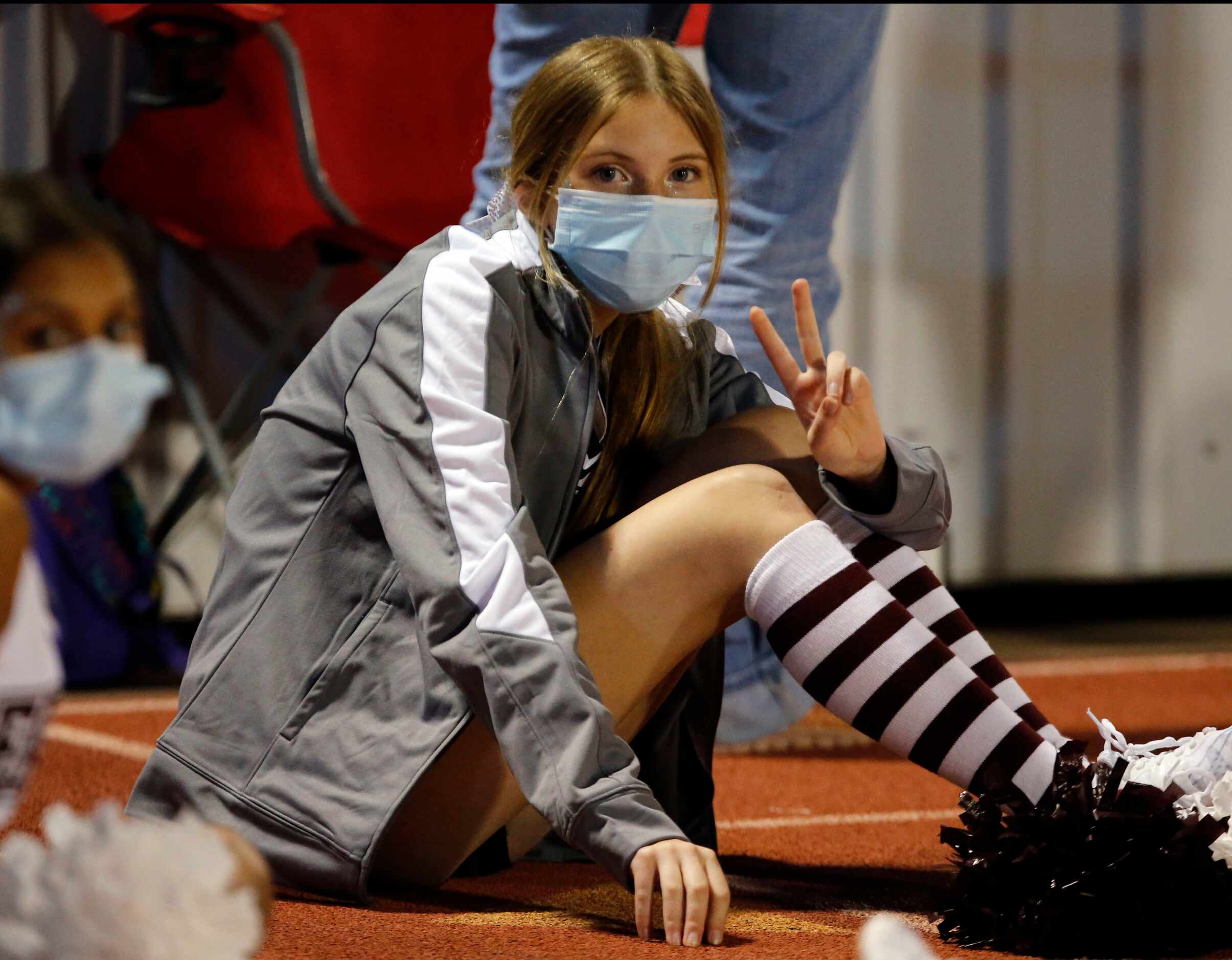 A mask-clad Rowlett cheerleader waves at the camera before the start of high school football...