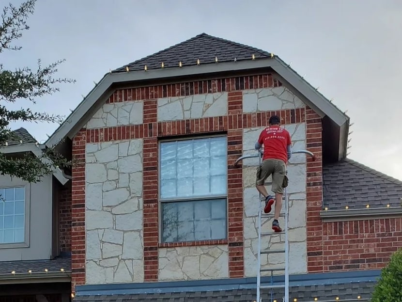 Man on ladder hanging Christmas lights on a home