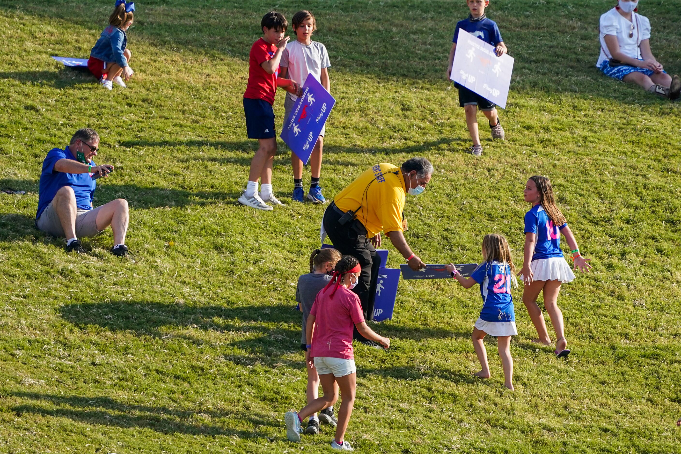 A stadium official collects social distancing signs from children who were using them to...