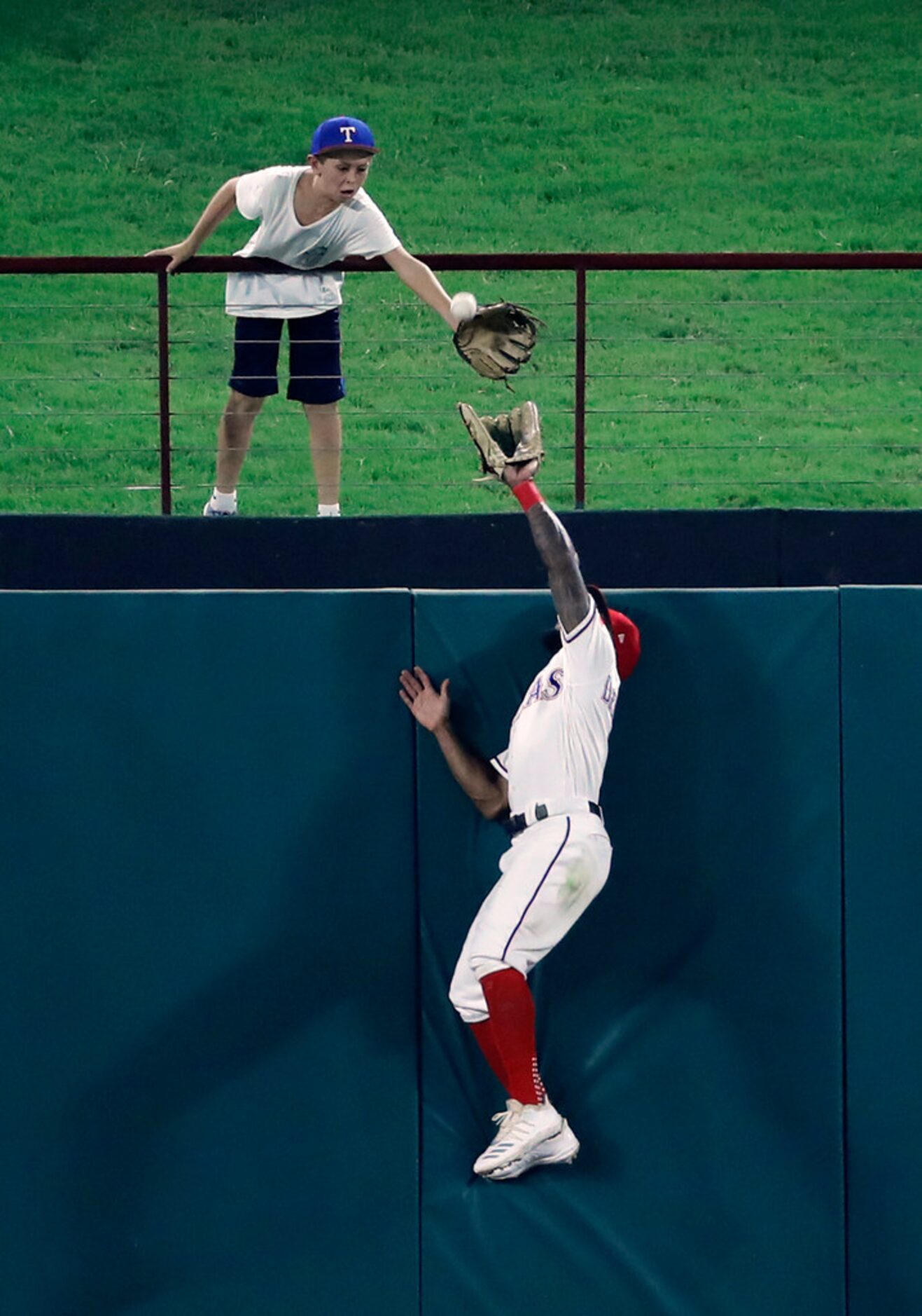 A young fan and Texas Rangers center fielder Delino DeShields reach up attempting to reach...