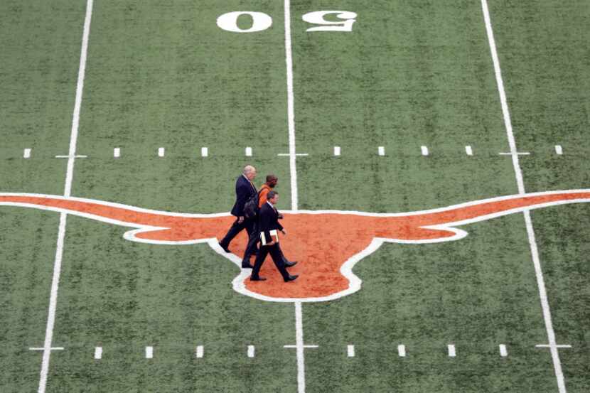 Tom Herman, front, walks across the Texas logo at Texas Memorial Stadium with associate...