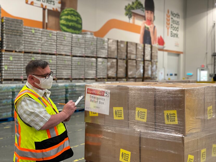 A masked man in a warehouse examines boxes taped together for Nourish North Texas.