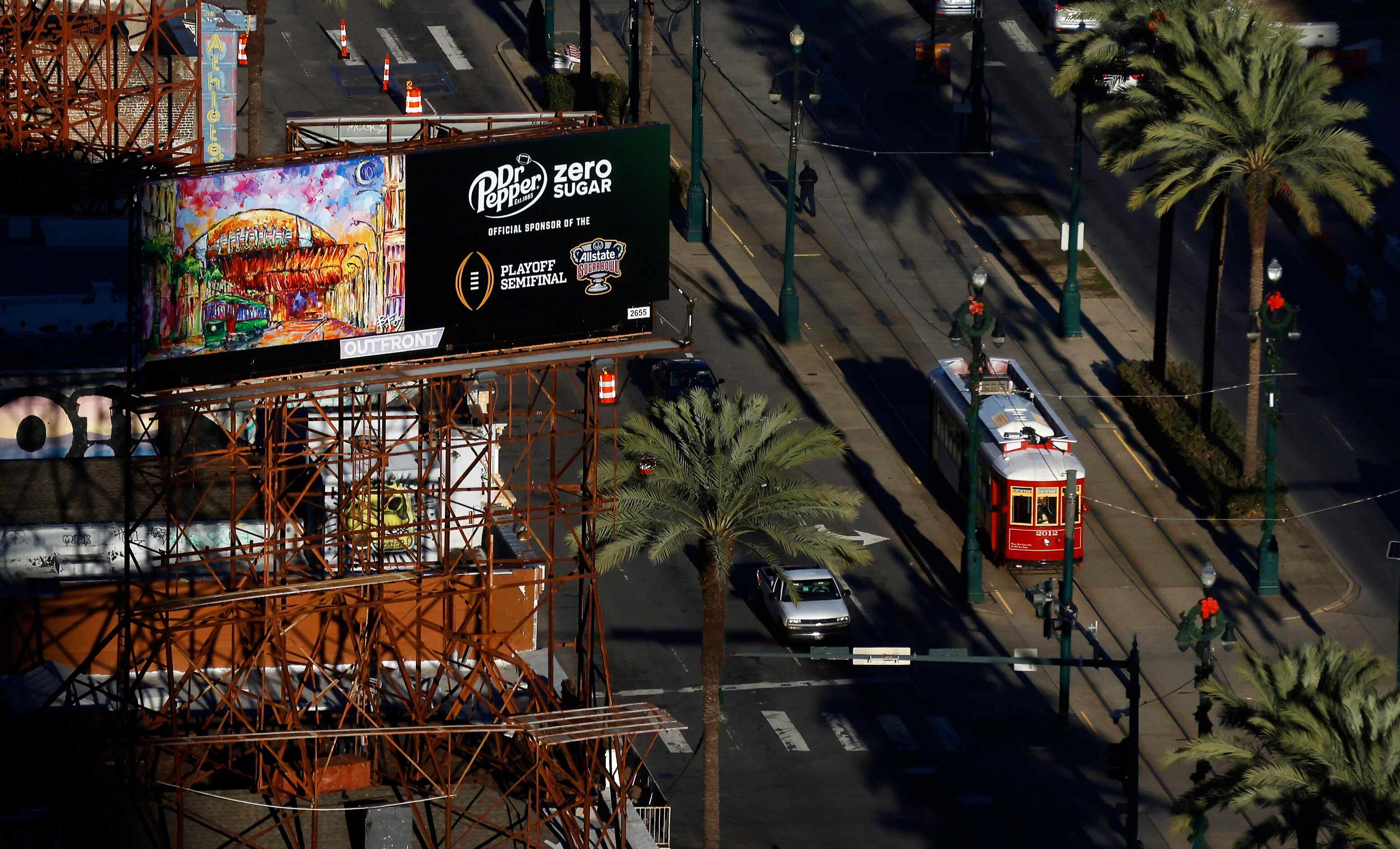 A streetcar runs along Canal St past a billboard advertising the College Football Playoff...