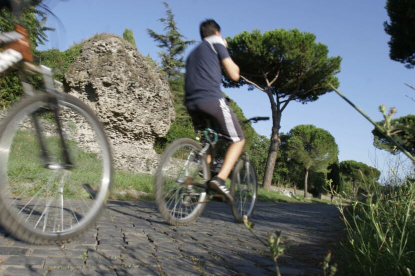 In this Sept. 7, 2013 photo, people cycle past ruins along the Appia Antica, the ancient...