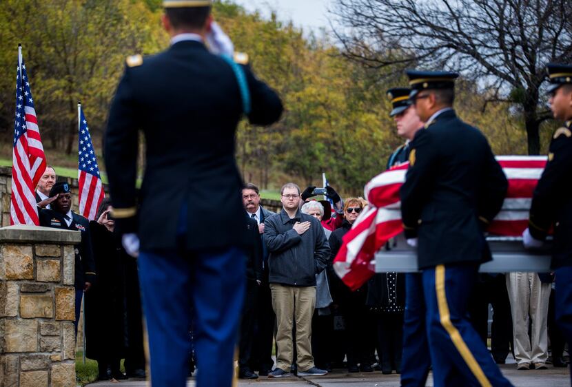 Family members watch as members of the Army Honor Guard carry a casket containing the...