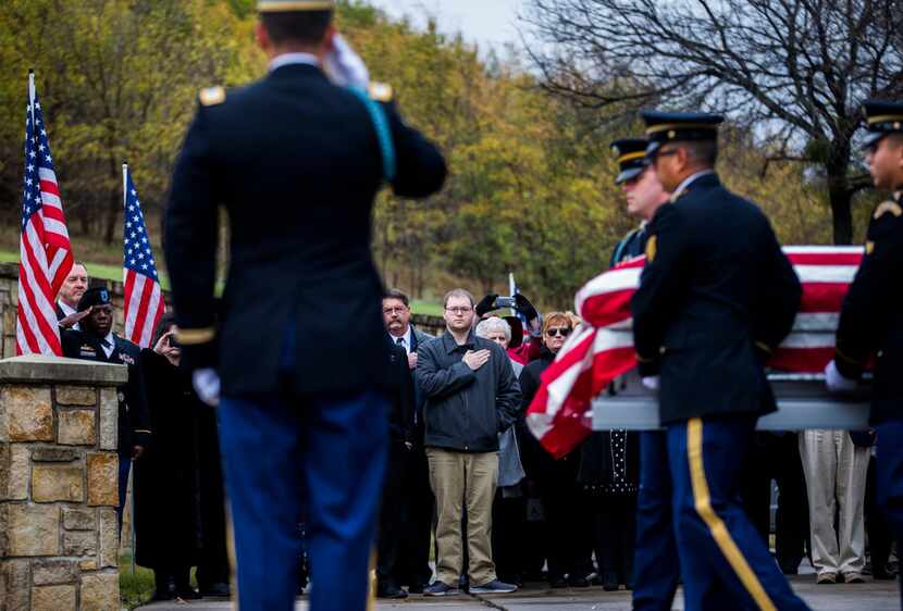 Family members watch as members of the Army Honor Guard carry a casket containing the...