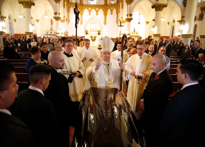 Bishop Kevin J. Farrell sprinkles Holy Water on the casket before leading a funeral mass for...